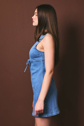 Side view of woman wearing a blue denim dress against a brown background