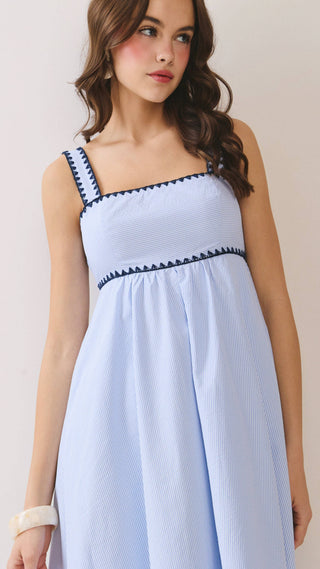 Woman wearing a light blue dress with black trim against a plain background
