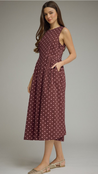 Round neckline sleeveless crimson dress with pink polka dots a gathered waist forming waist with an A-line pleated midi skirt