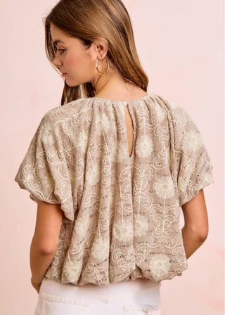 Woman wearing a beige lace embroidered bubble hem puff sleeved louse