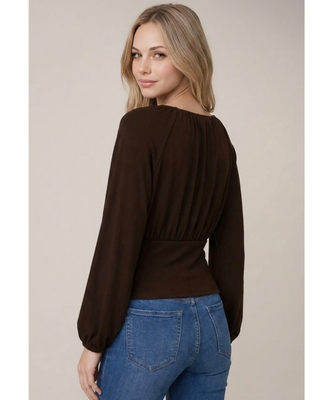 Woman wearing a chocolate brown long sleeve blouse with a gathered round neckline, ruched waist, fitted waistband, and balloon sleeves, paired with blue jeans.