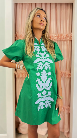Woman wearing an emerald green embroidered shift dress with white appliqué detailing and puff sleeves, styled for a chic boutique fashion look.