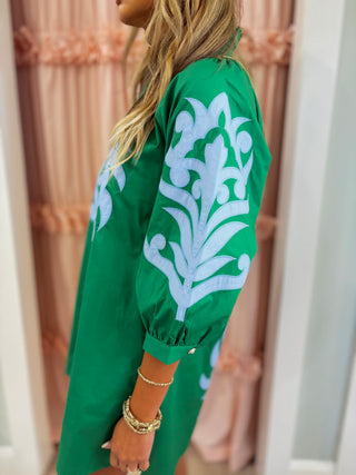 Woman wearing an emerald green embroidered shift dress with blue appliqué detailing and puff sleeves, styled for a chic boutique fashion look.