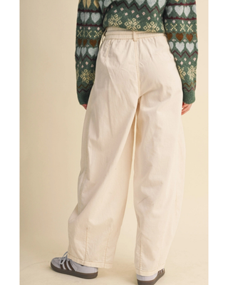 A person shown from the back wearing wide-leg cream pants, a green patterned knit sweater, and gray sneakers against a plain beige studio background.