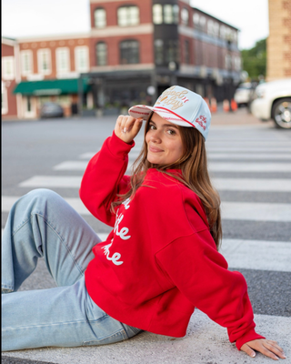Woman wearing the It’s a Good Day for Baseball Trucker Hat with a red sweatshirt and jeans.