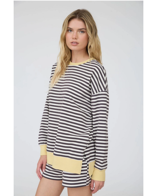 A woman modeling a matching lounge set consisting of a long-sleeve top and shorts in a gray and white horizontal stripe pattern with yellow ribbed trim.