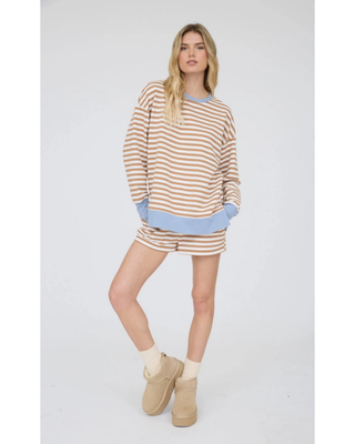 A woman modeling a matching lounge set consisting of a long-sleeve top and shorts in a beige and white horizontal stripe pattern with light blue ribbed trim.
