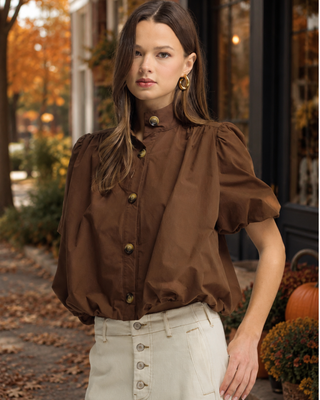 Women's chocolate brown puff sleeve blouse with a high neckline, tortoise-style button front, and relaxed fit styled with cream pants.