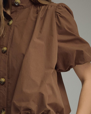 Women's chocolate brown puff sleeve blouse with a high neckline, tortoise-style button front, and relaxed fit styled with cream pants.