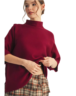Women’s burgundy mock neck sweater top with elbow-length sleeves styled with a plaid pleated skirt.