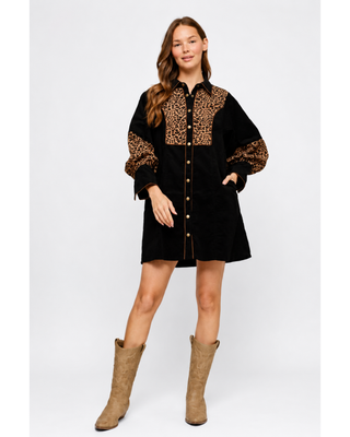 Woman wearing a black button-front mini shirt dress with leopard print chest and sleeve panels, gold-tone buttons, side pockets and tan western boots.