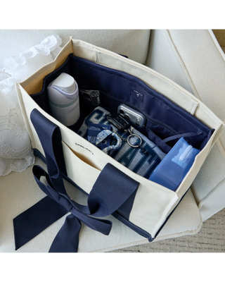 Navy blue tote bag organizer insert with multiple interior pockets holding a water bottle, phone, sunglasses, cosmetics, and everyday essentials.