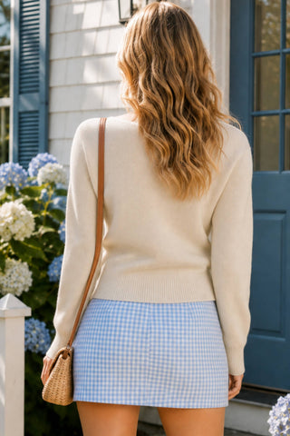 Women's ivory knit button-front cardigan with open collar, long sleeves and ribbed trim, styled with a blue gingham mini skirt.