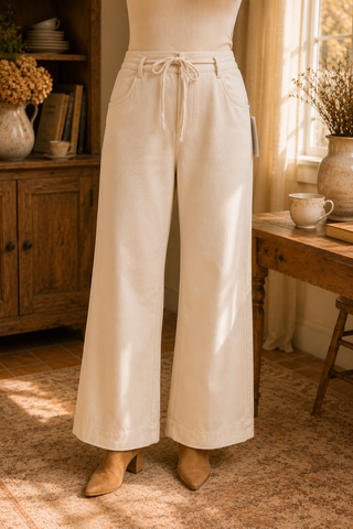 Women's ivory high-rise wide leg pants with adjustable drawstring waist and side pockets, styled with a fitted cream ribbed top and ankle boots.