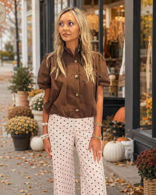 Women's chocolate brown puff sleeve blouse with a high neckline, tortoise-style button front, and relaxed fit styled with cream pants.