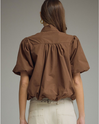 Women's chocolate brown puff sleeve blouse with a high neckline, tortoise-style button front, and relaxed fit styled with cream pants.