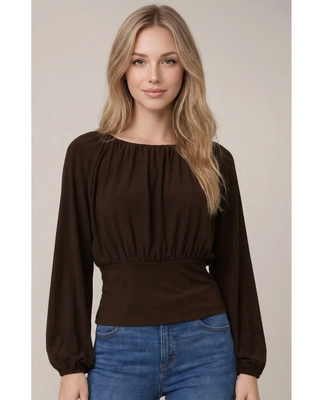 Woman wearing a chocolate brown long sleeve blouse with a gathered round neckline, ruched waist, fitted waistband, and balloon sleeves, paired with blue jeans.