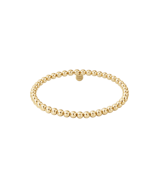 Close-up of a delicate metallic beaded bracelet worn on the wrist with a neutral stone background.