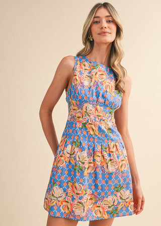 Woman wearing a colorful floral pleated waist mini dress against a beige background