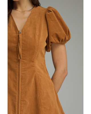 Woman wearing a camel brown corduroy mini dress with short puff sleeves, V-neckline, fitted waist and A-line skirt.