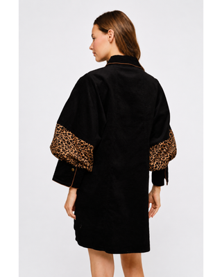 Woman wearing a black button-front mini shirt dress with leopard print chest and sleeve panels, gold-tone buttons, side pockets and tan western boots.