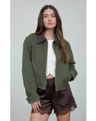 Woman wearing an olive green cropped utility jacket with a dark brown contrast collar, front zipper, and long sleeves over a white top.