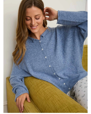 Woman wearing a soft blue knit button-front cardigan with a small collar and long sleeves, styled with white floral print bottoms.