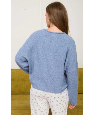 Woman wearing a soft blue knit button-front cardigan with a small collar and long sleeves, styled with white floral print bottoms.