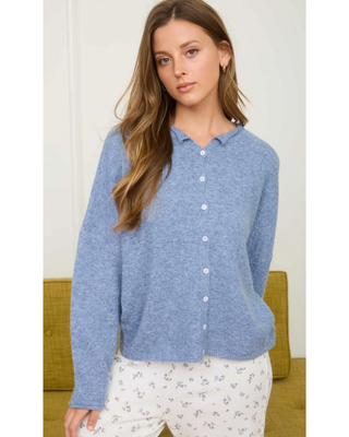 Woman wearing a soft blue knit button-front cardigan with a small collar and long sleeves, styled with white floral print bottoms.

