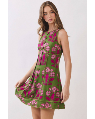 Woman wearing an olive green sleeveless fit-and-flare mini dress with vibrant fuchsia floral jacquard detailing, styled for weddings, brunches, and garden parties.