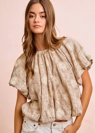 Woman wearing a beige lace bubble blouse against a pink background