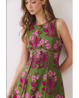 Woman wearing an olive green sleeveless fit-and-flare mini dress with vibrant fuchsia floral jacquard detailing, styled for weddings, brunches, and garden parties.