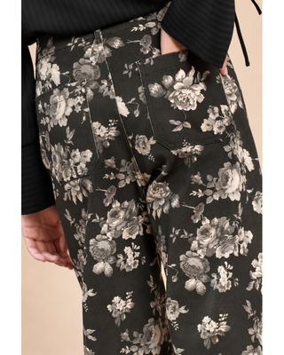 Close-up of a person wearing black wide-leg pants with a gray and beige floral print, paired with a black ribbed long-sleeve top against a light beige background.