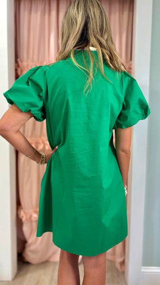 Woman wearing an emerald green embroidered shift dress with white appliqué detailing and puff sleeves, styled for a chic boutique fashion look.