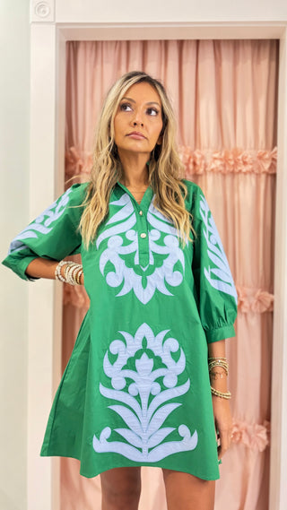 Woman wearing an emerald green embroidered shift dress with blue appliqué detailing and puff sleeves, styled for a chic boutique fashion look.