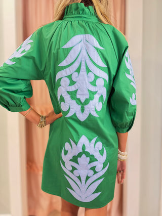 Back view of Woman wearing an emerald green embroidered shift dress with blue appliqué detailing and puff sleeves, styled for a chic boutique fashion look.