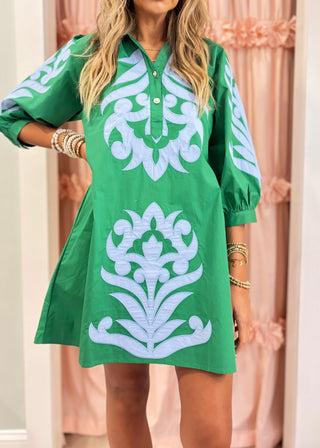 Woman wearing an emerald green embroidered shift dress with blue appliqué detailing and puff sleeves, styled for a chic boutique fashion look.