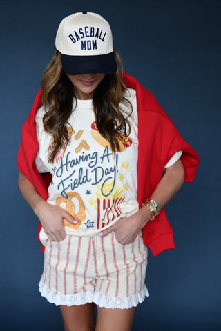 Woman modeling the Having a Field Day graphic tee with red striped lace-trim shorts, a red cardigan, and a Baseball Mom cap.