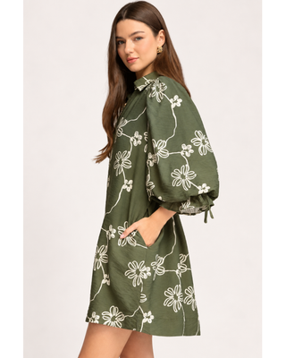 Olive green floral mini dress with cream abstract flower print, collared V-neckline, balloon sleeves with tie cuffs, and side pockets.