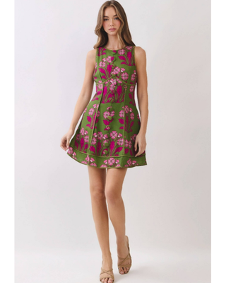 Woman wearing an olive green sleeveless fit-and-flare mini dress with vibrant fuchsia floral jacquard detailing, styled for weddings, brunches, and garden parties.