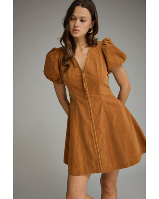 Woman wearing a camel brown corduroy mini dress with short puff sleeves, V-neckline, fitted waist and A-line skirt.