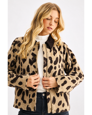 Woman wearing a taupe and dark brown leopard print zip-front jacket with a contrasting brown collar and pocket trim, styled with a white top and dark denim jeans.