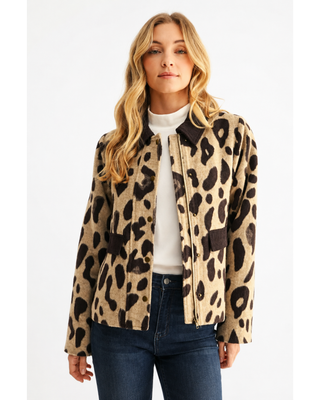 Woman wearing a taupe and dark brown leopard print zip-front jacket with a contrasting brown collar and pocket trim, styled with a white top and dark denim jeans.
