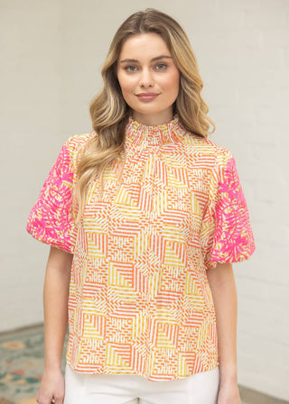 Woman wearing a colorful patterned blouse with a neutral background