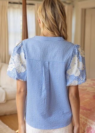Woman wearing a blue and white checkered blouse with floral sleeves in a room.