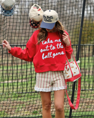 Woman modeling the red Madison Take Me Out to the Ball Game Sweatshirt with a white baseball-inspired graphic.