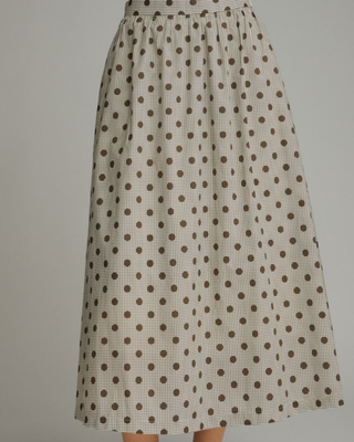Women's mocha polka dot A-line midi skirt with a high-rise waistband and flowy silhouette in a lightweight woven fabric, styled for an elegant boutique look.