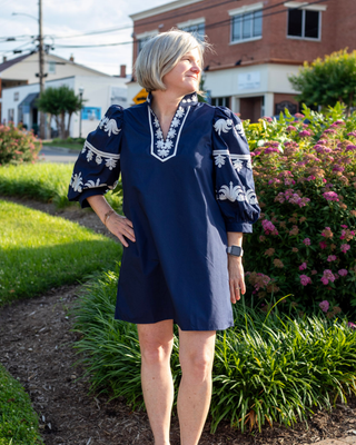 Woman wearing a navy embroidered puff sleeve shift dress with white embroidered detailing on the neckline and sleeves.