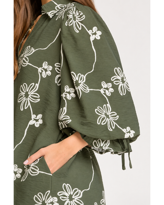 Olive green floral mini dress with cream abstract flower print, collared V-neckline, balloon sleeves with tie cuffs, and side pockets.