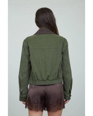 Woman wearing an olive green cropped utility jacket with a dark brown contrast collar, front zipper, and long sleeves over a white top.